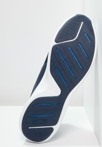 Navy tenisky s texturovanou gumovou podrážkou, bílou mezipodrážkou a modrými akcenty. Disponují vroubkovanými vzory pro trakci a odolnost.