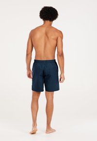 Shorts de bain bleu marine avec une taille élastique et une coupe décontractée, fabriqués en tissu léger, montrés de dos.