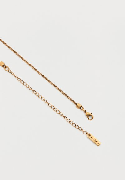 Κολιέ αλυσίδας σε χρυσό τόνο με κούμπωμα τύπου αστακού και ρυθμιζόμενη αλυσίδα, με ορθογώνια ταμπέλα "VERSACE" σε λευκό φόντο.