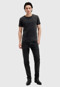 Schwarzes Baumwoll-T-Shirt mit Rundhalsausschnitt, kombiniert mit dunkelgrauen Jeans. Das Outfit wird durch schwarze Stiefeletten ergänzt.