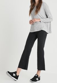Graues langärmeliges Oberteil mit lockerer Passform, kombiniert mit schwarzen, knöchellangen Jeans und schwarzen Turnschuhen mit einem weißen Logo. Schlichtes Design und weicher Stoff.