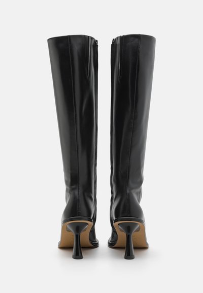 Svarta knähöga stövlar i glättad läder, med en slank design, spetsig tå och en böjd stilettklack. Dragkedja i ryggen.