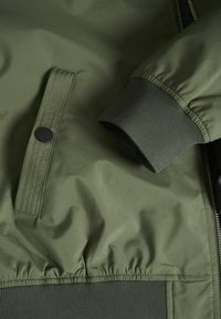 Olive green bomber jacket with a smooth, shiny texture, featuring a ribbed cuff and elastic waistband, and a snap-button pocket.