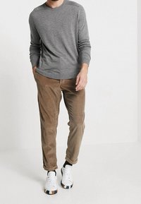 Grå stickad långärmad tröja ihop med ljusbruna kordflorsbyxor. Modellen bär vita sneakers med en färgad rand på sulan.