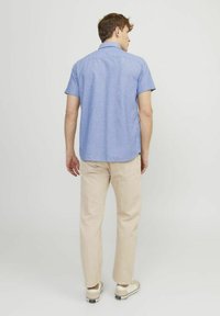 Korte mouwen, lichtblauwe button-up overhemd met een gestructureerd patroon, gecombineerd met beige broek en lichtgekleurde schoenen. Achteraanzicht.