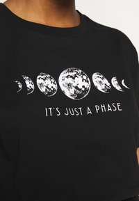 Camiseta de algodón negra con cuello redondo que presenta un gráfico blanco de diferentes fases de la luna y el texto "SOLO ES UNA FASE" abajo.