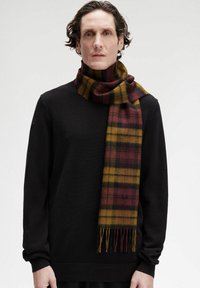 Sciarpa di lana a quadri in bordeaux scuro, giallo e nero, con bordi frangiati, indossata sopra un maglione nero texturizzato.