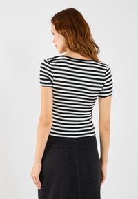 Svart-hvite stripete kortermet topp, ribbestruktur, tettsittende design, sett fra baksiden, kombinert med en mørk denimskjørt.