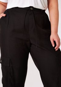 Schwarze Cargo-Hosen aus robustem Material mit verstellbarem Gummizug, seitlichen Taschen und Druckknopf-Akzenten. Entspannter Schnitt.