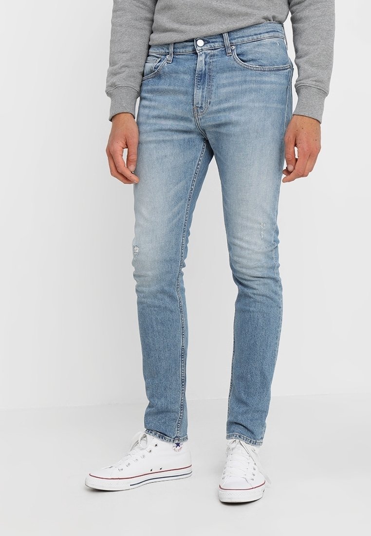 Ljusblå denimjeans med slim fit, med en blekt tvätt och subtila slitningar. Bärs med en grå sweatshirt och vita sneakers.