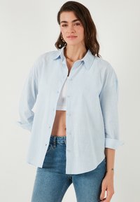 Camicia button-up azzurro chiaro con colletto classico, maniche lunghe e vestibilità rilassata. Realizzata in un tessuto leggero con una superficie liscia.