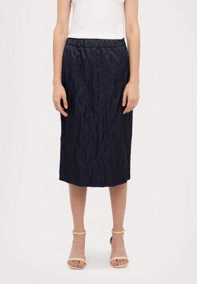 Navy, knee-length skirt with a textured, crinkled fabric. Elastic waistband and a straight cut, paired with light yellow strappy sandals.