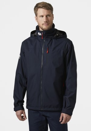 Navyblauwe waterdichte jas met een capuchon, ritssluiting aan de voorkant, rode ritsaccenten, verstelbare manchetten en logo op de schouder.