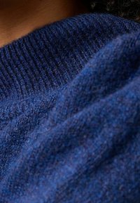 Pull en tricot bleu marine avec col côtelé et tissu doux et texturé. Le matériau semble chaud avec une finition légèrement duveteuse.