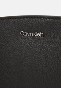 Pezzo di pelle nera testurizzata con il logo "Calvin Klein" in argento. Superficie liscia con un evidente motivo di grana.