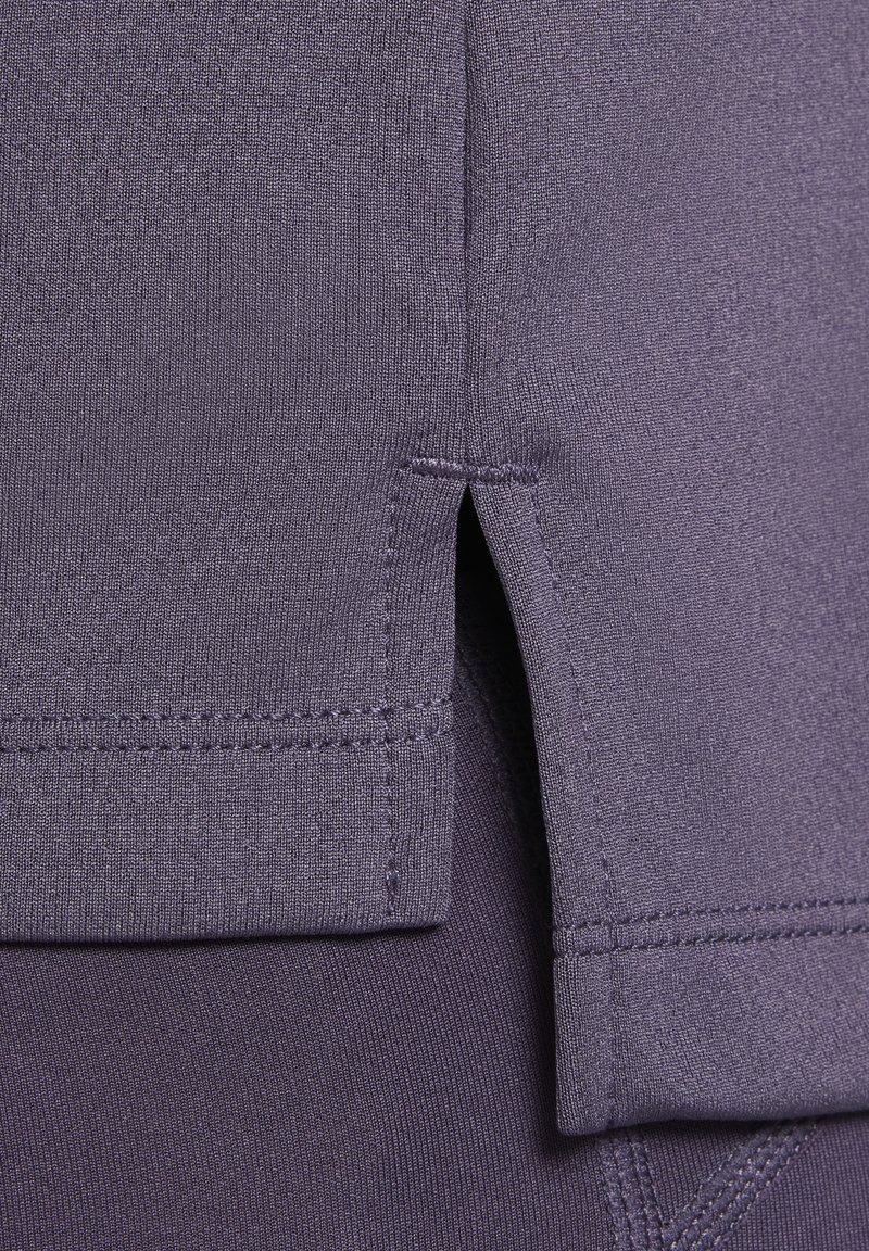 Tessuto di maglietta atletica viola con una texture liscia, caratterizzata da uno spacco laterale e cuciture piatte per una vestibilità contemporanea. Nessun marchio o motivo visibile.