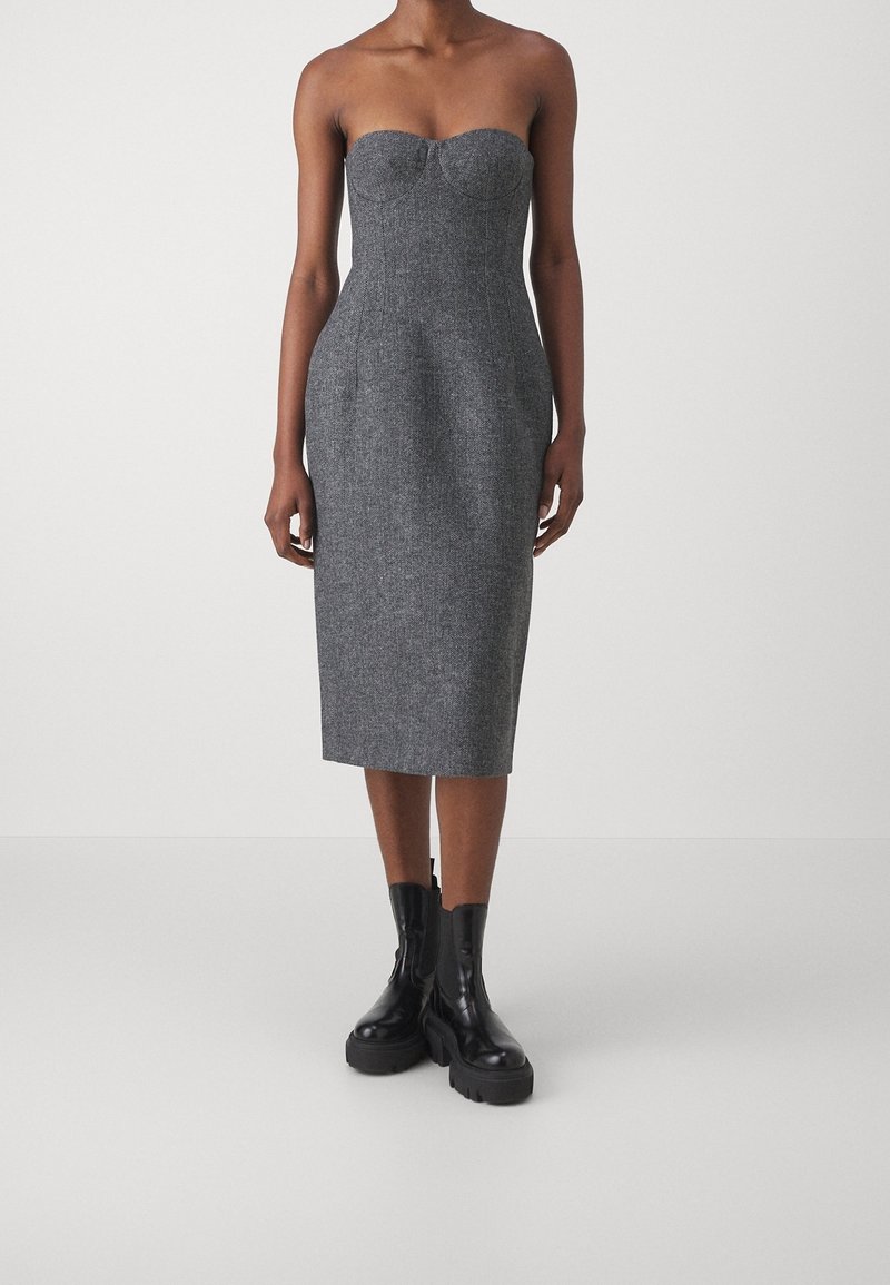 Robe grise sans bretelles en tissu texturé, cintrée et longueur genou, avec un décolleté en forme de cœur et un corsage structuré, portée avec des bottes noires.