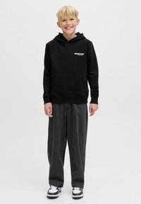Felpa nera con cappuccio e tasca davanti, con logo bianco. Abbinata a pantaloni grigi scuri larghi e sneakers bianco e nere.