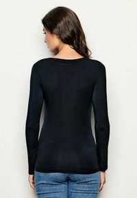 Maglietta nera a maniche lunghe con scollatura rotonda, forma aderente e texture liscia, abbinata a jeans blu, vista da dietro.