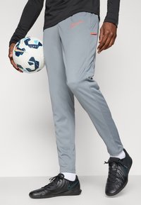 Light grey athletic pants with a slim fit, black Nike shoes, and a soccer ball featuring blue and black accents. Orange Nike logo prominent.