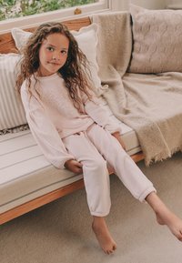 Set di abbigliamento da casa rosa chiaro realizzato in tessuto morbido, con motivo a cuore sulla maglia e polsini elastici sui pantaloni.