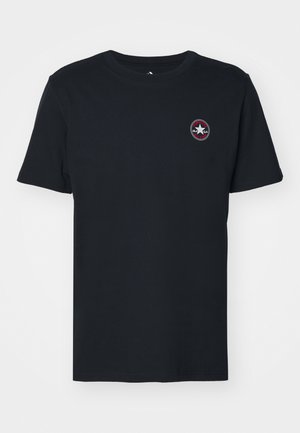 Czarna koszulka z krótkim rękawem i okrągłym dekoltem, z małym, okrągłym logo Converse w białym i czerwonym kolorze na lewej stronie klatki piersiowej.