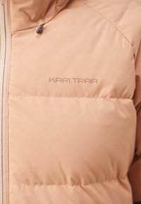 Dámska prešívaná bunda Kari Traa v svetlo broskyňovej farbe s hladkou textúrou, so zapínaním na zips a diskrétnym logom na hrudi.