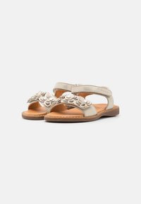 Sandales en cuir beige avec des embellissements floraux, une sangle réglable, un design à bout ouvert et une semelle en caoutchouc texturé marron.