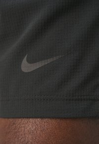 Shorts de sport noirs avec un motif de grille texturé et un logo Nike gris subtile en bas à gauche.