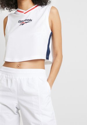 Top corto blanco sin mangas con logo de Reebok, con detalles en rojo y azul marino y diseño de escote en V. Combinado con pantalones blancos de cintura elástica.