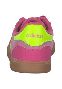Tenisky Adidas v ružovej a neónovo žltej z semišu, s gumenou podšívkou a polstrovaným golierom. Obsahujú logo na päte a perforovanú textúru.
