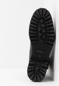 Semelle de botte noire en caoutchouc avec un motif de bande de roulement texturé, comportant des rainures d'adhérence prononcées et le nom de la marque en relief. Taille indiquée : 39.