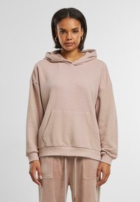 Myk, oversized rosa hettegenser med en frontlomme, snorhette og ribbet ermer. Stoffet ser teksturert og glatt ut.