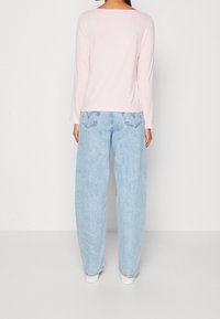 Rosa Langarmshirt, kombiniert mit hellblauen, locker sitzenden Jeans. Die Jeans haben traditionelle Gesäßtaschen und umgeschlagene Bündchen.