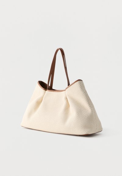 Τσάντα tote με κρεμ υφή, καφέ δερμάτινες λαβές και επένδυση, εμφανίζεται σε απλό λευκό φόντο.