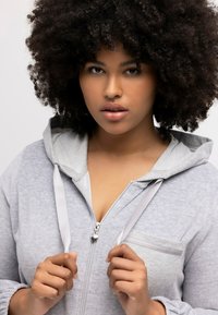Hellgraue Zip-Hoodie mit einer Kapuze mit Zugband, Fronttasche und kontrastierenden grauen Akzenten. Weiches, strukturiertes Gewebe mit einer lässigen Passform.
