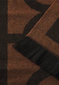 Wollschal in Braun mit geometrischem Muster. Verfügt über einen schwarzen Fransenbesatz an einer Kante. Weiche Textur, warmes Erscheinungsbild.