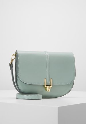 Petit sac bandoulière en cuir vert pastel avec fermoir doré et bandoulière détachable, présenté sur une surface blanche.