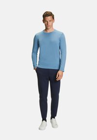 Maglione a maniche lunghe azzurro chiaro in morbido knit, abbinato a pantaloni blu navy e sneaker bianche, con scollatura a girocollo e design aderente.
