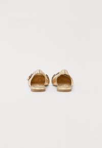 Sandales à glissière métalliques dorées avec un dos ouvert et un design découpé décoratif sur les sangles. Texture lisse, semelles plates et style minimaliste.