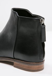 Czarne skórzane botki za kostkę o gładkiej fakturze, niskim obcasie i bocznym suwak. Posiadają drewnianą podeszwę oraz uchwyt, który ułatwia zakładanie.