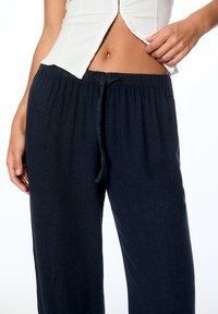 Ciemnoniebieskie, lekkie spodnie lniane z elastycznym pasem, sznurkiem i luźnym krojem. Gładka faktura, idealne do noszenia na co dzień.