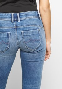 Smala blå denimjeans med medelhög midja. Har två bakfickor med svängd sömnad och en slät textur.