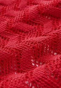 Tissu tricoté rouge avec une texture en dentelle ouverte, affichant un motif en treillis et une apparence douce légèrement duveteuse.