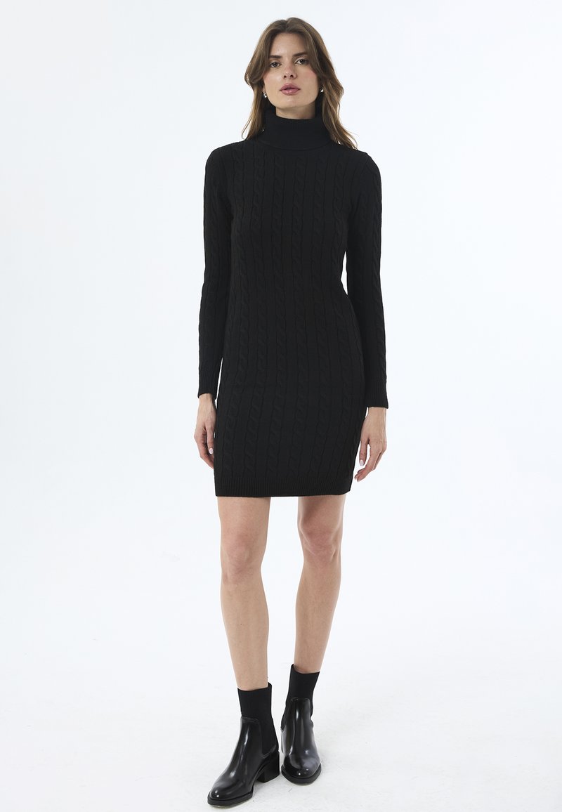 Mustmustriivne must kleit kõrge kaelusega, millel on nöörkootud muster ja pikad varrukad, koos mustade pahkluu saapadega.