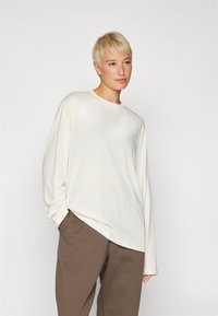 Langermet kremfarget skjorte i mykt stoff med en litt oversized passform, med rund hals og en subtil logo på brystet.