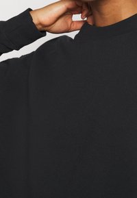 Primo piano di una persona che aggiusta il colletto di una camicia nera a maniche lunghe con la mano destra vicino al collo.