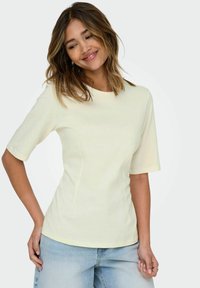 Chemise jaune clair à manches courtes avec un col rond, design ajusté et texture de tissu lisse, accompagnée d'un pantalon en jean taille haute bleu clair.