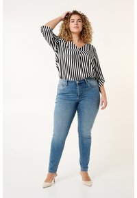Zwart-wit gestreepte blouse met lange mouwen en v-hals, gecombineerd met lichtblauwe skinny jeans. Het model draagt huidskleurige hakken.