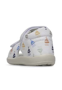 Witte sandalen met een patroon van kleurrijke zeilbootjes, voorzien van een klittenbandsluiting en een open ontwerp. Voetbed van gestructureerd beige rubber voor grip.